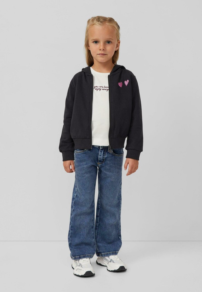 Tamsiai pilkas užtrauktuku užsegamas džemperis su dviem rožinėmis širdelėmis, balta marškinėliai su užrašu, mėlyni plačios kojos džinsai ir balti sportbačiai.