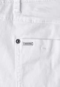 Tissu blanc en gros plan montrant une poche avec un bouton métallique et une petite étiquette rectangulaire de la marque "Street One".
