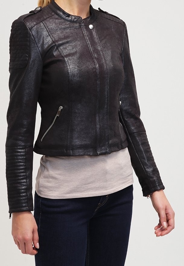 Kobieta w dopasowanej czarnej skórzanej kurtce z zamykanymi kieszeniami oraz pikowanymi detalami na ramionach i rękawach, w zestawieniu z ciemnymi dżinsami i beżową bluzką.