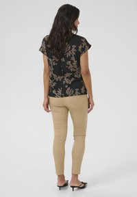 Blusa nera floreale con maniche corte, caratterizzata da dettagli dorati; pantaloni beige a sigaretta; mule nere con tacco; trame lisce in tutto l'outfit.