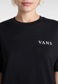 Černé bavlněné tričko s kulatým výstřihem a bílým logem "VANS" na horní části levé části hrudi. Hladká textura.