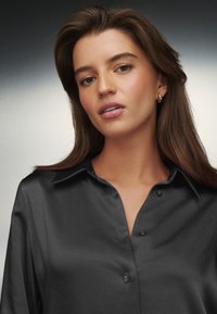 Schwarzes Satinhemd mit Kragen und durchgehender Knopfleiste. Es zeichnet sich durch eine glatte Textur und dezenten Glanz aus, mit schwarzen Knöpfen und lockerem Sitz.