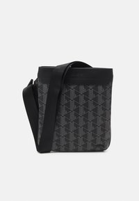 Bolso negro con patrón geométrico hecho de tela texturizada, con correa negra y cierre superior. Logotipo de Lacoste estampado en el frente.