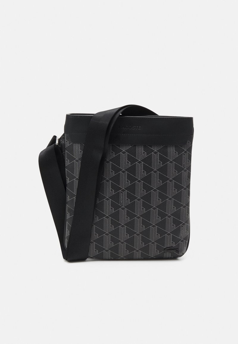 Bolso negro con patrón geométrico hecho de tela texturizada, con correa negra y cierre superior. Logotipo de Lacoste estampado en el frente.