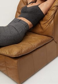 Haut gris ajusté et pantalon taille haute à carreaux, reposant sur un canapé en cuir brun texturé, mettant en valeur sa surface douce et froissée.