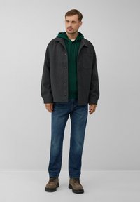 Grijze wollen jas met knopen, groene hoodie eronder, blauwe spijkerbroek en bruine laarzen. Eenvoudig ontwerp met een voorkant zak op de jas.