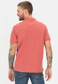 Korte mouwen polo shirt voor heren in koraal, gemaakt van lichte stof. Het heeft een klassieke kraag en een gestikte zoom met zijsplitten.