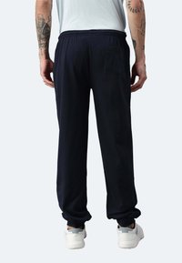 Navyblaue Jogginghosen aus weichem Stoff, mit einem elastischen Bund, schmal zulaufenden Bündchen und einer Rückentasche. Tragen Sie sie zu weißen Sneakern.
