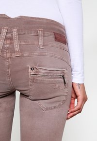 Jeans de mezclilla rosa claro con una cintura alta, un bolsillo trasero con cremallera y un pequeño detalle bordado encima del bolsillo.