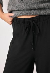 Black elastic waistband pants with adjustable drawstring, featuring a smooth texture and side pockets. Paired with a grey fuzzy sweater.