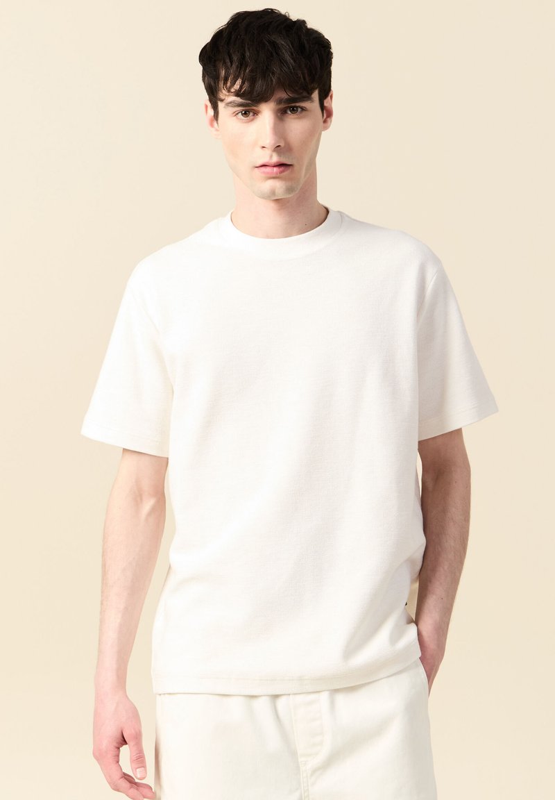 Vit t-shirt med kort ärm i sträv väv, med rund halsringning och avslappnad passform. Enkelt design utan synliga mönster.