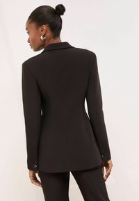 Fekete szabott blézer struktúrált sziluettel, kivágott gallérral és gombos mandzsettával, hátulról bemutatva sima felülettel.