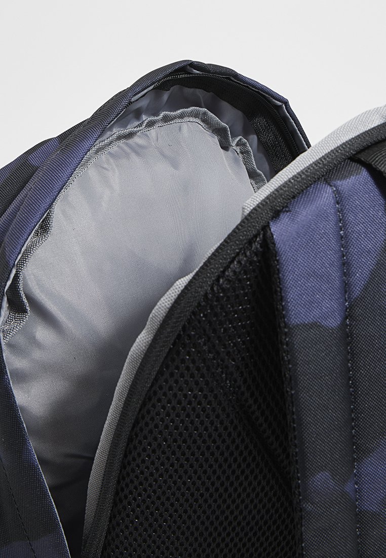 Rucksack mit navyfarbener Camouflage-Außenfläche, grauem Innenfutter, gepolstertem Innenraum und Mesh-Akzenten für Belüftung. Mit einem abgebildeten Reißverschlussverschluss.