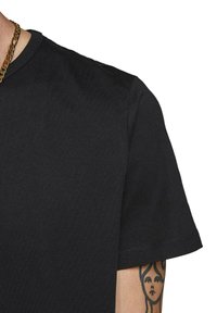 T-shirt in cotone nero con collo rotondo, maniche corte e una superficie liscia. Presenta un tatuaggio visibile sul braccio.