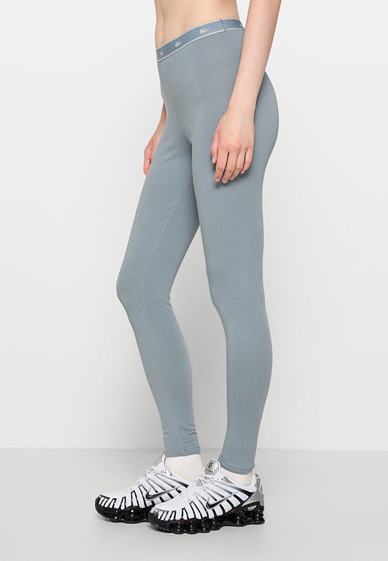 Leggings de color azul claro con una textura suave y una cintura alta, combinados con zapatillas de deporte blancas y negras que presentan un diseño único.