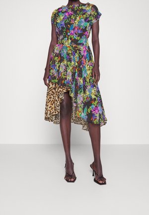 Femme portant une robe asymétrique à imprimé floral et léopard avec un ourlet à volants, associée à des sandales noires à lanières et talons hauts.