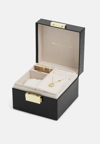 Schmuckkästchen in Schwarz mit strukturiertem Äußeren, goldenen Beschlägen und weichem beigen Innenraum. Enthält Fächer für Ohrringe und eine Anhänger-Halskette.