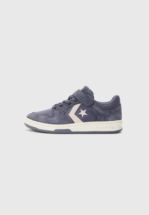 Barnas marineblå Converse-sneaker med hvitt stjernelogo, borrelås, snørebånd og hvit såle mot en enkel lys bakgrunn.
