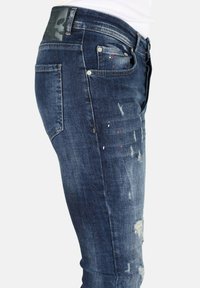 Vervaagde donkerblauwe spijkerbroeken van denim met beschadigingen en verfspetters, in een aansluitende vorm met metalen hardwaredetails.