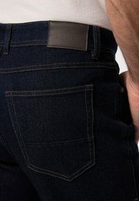 Granatowe d żinsy z denimu z skórzaną naszywką z napisem "BOSTON PARK" w pasie, kontrastującym złotym przeszyciem i tylnymi kieszeniami.