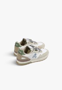 Zapatillas deportivas que combinan cuero blanco y gamuza beige, cordones grises, acentos verdes y un logo de calavera en el lado exterior.