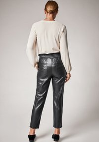 Pantalons en cuir noir avec une taille élastique et deux poches arrière, associés à un chemisier beige clair à manches longues.