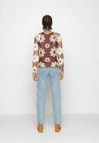 Camisola transparente de mangas longas em bordeaux com grande padrão floral branco; usada com jeans de ganga azul claro e sapatos de salto bloco em tom de areia.