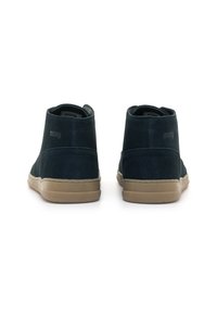 Stivali alla caviglia in suede blu navy con superficie texture, suola in gomma color tan e branding discreto sul tallone. Fodera liscia, design minimalista.