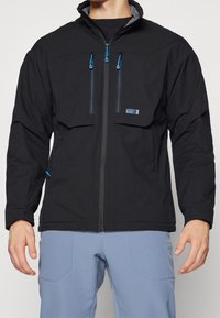 Veste noire dotée de deux poches poitrine zippées avec des accents bleus, d'une fermeture éclair à l'avant et de poignets élastiques. Le tissu semble résistant à l'eau.