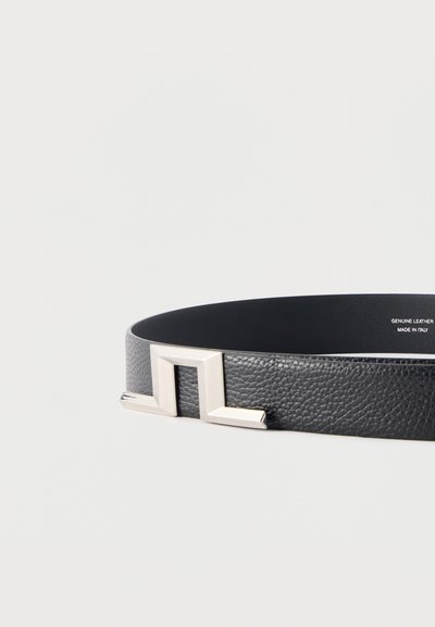 Μαύρη δερμάτινη ζώνη με υφή και χαρακτηριστική ασημένια γεωμετρική πόρπη, με ετικέτα γνήσιο δέρμα και κατασκευασμένη στην Ιταλία.