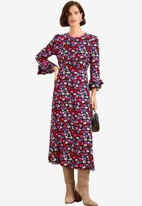 Rochie lungă florală cu un fundal negru și flori multicolore, cu mâneci volănașe și talie ajustată. Purtați cu cizme bej până la genunchi.