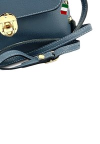 Blauwe leren schoudertas met gouden hardware, klepclosure, verstelbare schouderband en een charm van de Italiaanse vlag eraan bevestigd. Textuur, compacte uitstraling.