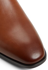 Zapato de cuero marrón con una textura suave, puntera puntiaguda y suela negra. Sin herrajes ni patrones visibles.