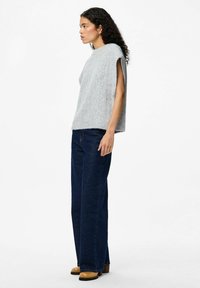 Grå stickad topp med en lös passform, med korta ärmar. Matchas med mörkblå vida jeans och bruna ankelstövlar.