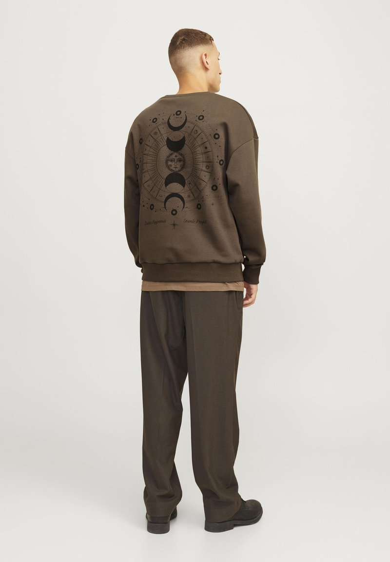 Sudadera marrón con un gráfico de la luna y el sol en la parte posterior. Corte holgado con puños y dobladillo acanalados. Llevada con pantalones marrones a juego.