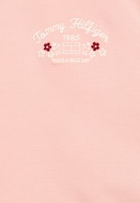 T-shirt di cotone rosa chiaro con ricamo del testo "Tommy Hilfiger 1985" con accenti floreali e la frase "HAVE A NICE DAY."