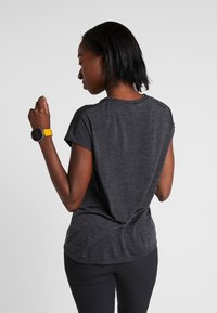 Charcoal gray t-shirt with short sleeves, soft texture, round neckline, and a slightly curved hem. Worn with black leggings and a yellow smartwatch.