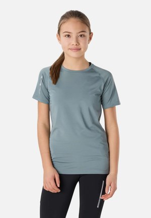 Jeune femme aux cheveux bruns attachés en queue de cheval, portant un t-shirt de sport bleu clair à manches courtes et un legging noir avec des détails réfléchissants.