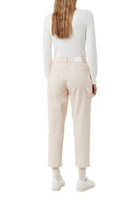 Jasnoróżowe bawełniane spodnie o luźnym kroju, z tylnymi kieszeniami i detalem w postaci pętli w pasie, zestawione z białymi butami i skarpetkami.