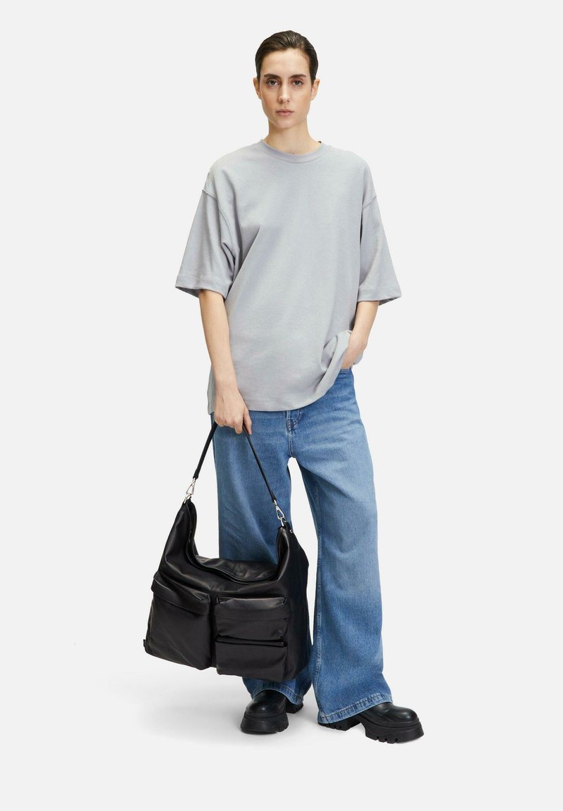 Graues oversized T-Shirt, hellblaue weite Jeans und eine schwarze Leder-Schultertasche mit zwei Fronttaschen. Weiche Texturen und minimalistisches Design.