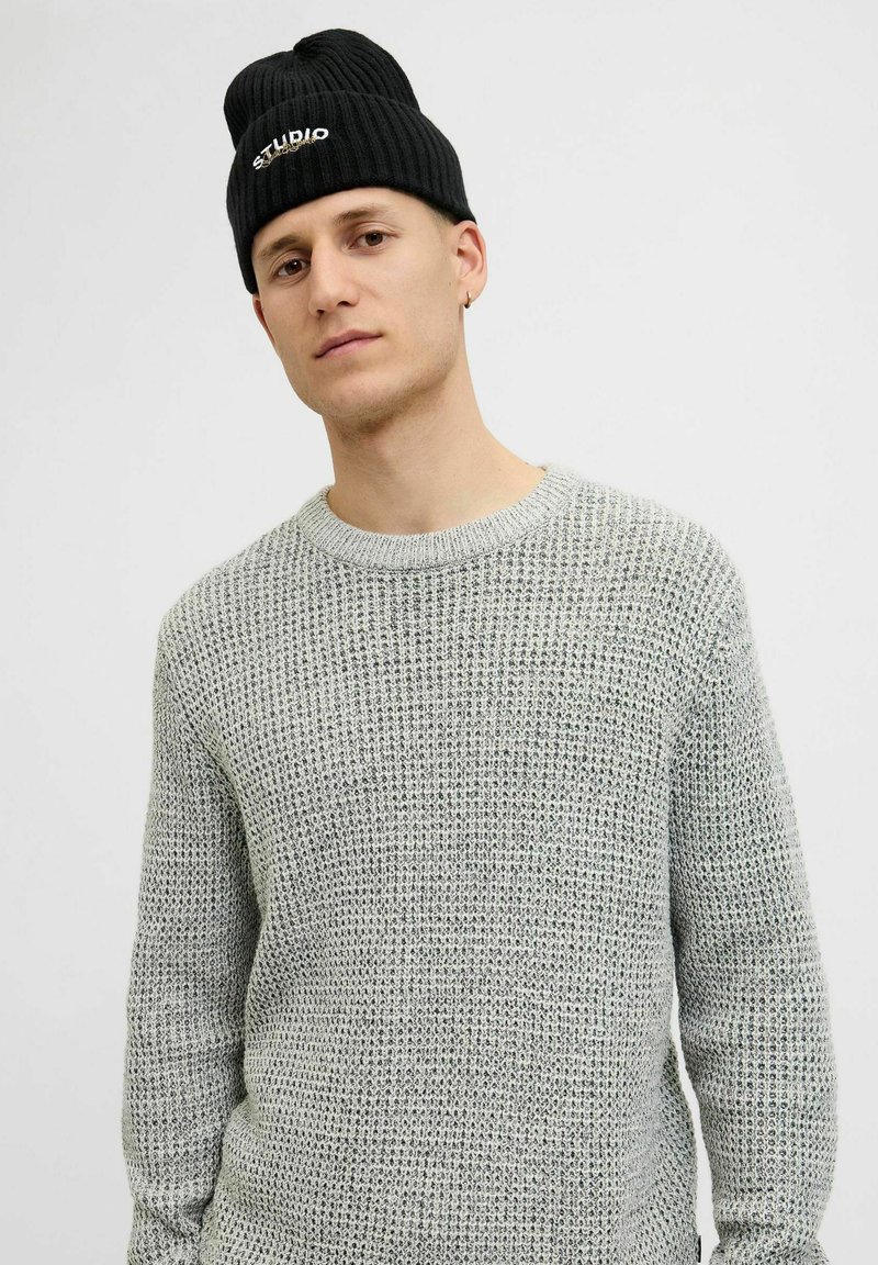 Lysegrå strikket sweater med et struktureret mønster, rund halsudskæring og lange ærmer. Kombineret med en sort ribbet beanie med hvidt logo.