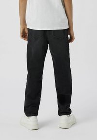 Jeans de mezclilla negra con corte recto, bolsillos traseros visibles y detalles de costura sutiles. Combinados con zapatillas blancas.