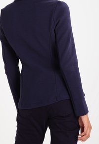 Námořnický texturovaný blazer s přiléhavým střihem, s mírně zakřiveným lemem a dlouhými rukávy. Hladká tkanina s minimálními detaily.