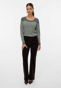 Haut à manches longues rayé en gris et blanc, associé à un pantalon évasé en velours côtelé marron foncé, avec une taille cintrée et une texture douce.