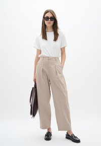 Beige wide-leg trousers with pleats, a white t-shirt, and black loafers. Accessories include black sunglasses and a dark brown tote bag.