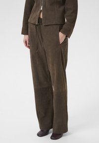 Bruine leren broeken met een losse pasvorm, een trekkoord in de taille en zijzakken. Zachte textuur met minimale stikdetails.