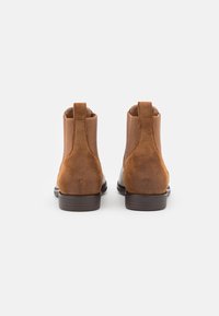 Bottes à chevilles en cuir marron avec des panneaux élastiques sur les côtés et des languettes, présentant une finition lisse et un talon empilé.
