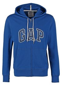 Felpa con zip blu, con cordini bianchi e grandi lettere GAP sul petto, dotata di tasche frontali e un'etichetta di taglia media all'interno del colletto.