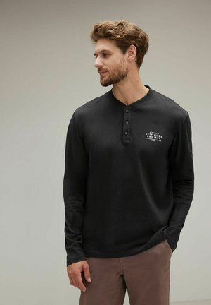Schwarzes Langarmshirt mit einem knöpfbaren Ausschnitt, das ein bedrucktes Logo auf der Brust trägt. Weicher Stoff mit einer taillierten Passform.