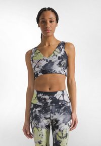 Sujetador deportivo tie-dye en negro y verde con diseño de cuello en V y tirantes anchos, combinado con leggings de talle alto a juego que presentan patrones similares.
